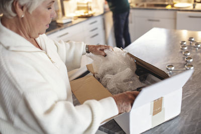 Side view of senior woman unpacking box on kitchen island at home