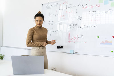 Woman looking at laptop while solving mathematical formula in living room