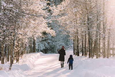 Rear view of mother and son walking in forest during winter