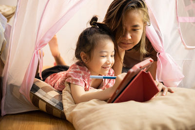 Face focusing on asian mom and adorable daughter are lying on the floor in pink tent at home