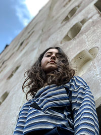 Low angle view portrait of young woman standing against wall