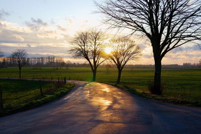 Road amidst bare trees against sky during sunset