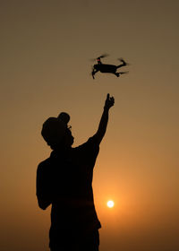 Silhouette man with arms raised standing against orange sky