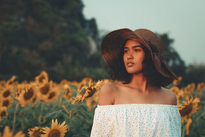 Woman in hat standing against flowering sunflowers