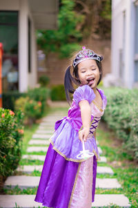 Girl wearing princess costume standing on footpath at back yard