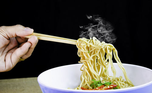 Cropped image of person having spaghetti with chopsticks against black background