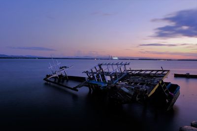 Abandoned boat on sea against sky during sunset