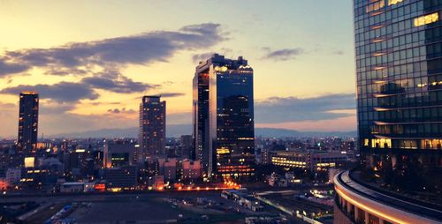 Illuminated buildings in city against sky during sunset