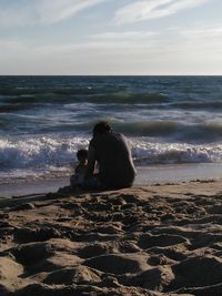 Rear view of man sitting on beach against sky