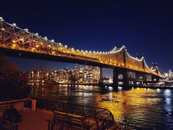 Illuminated bridge over river against sky at night