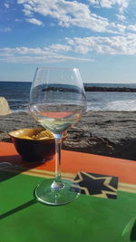 Close-up of wineglass on table by sea against sky