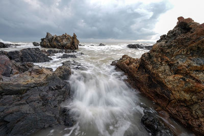 Long exposure image of waves crashing at beach against storm clouds