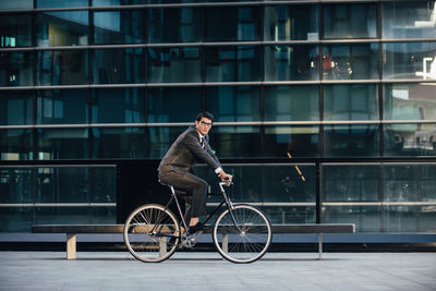 Man riding bicycle on glass building in city