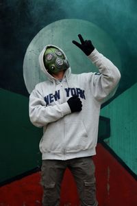 Man wearing gas mask showing peace sign while standing against wall