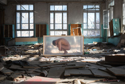 Naked mid adult man crouching in container at abandoned house