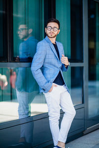 Full length portrait of young man leaning on glass wall