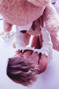 High angle view of sensuous woman lifting teddy bear while sitting on floor at home