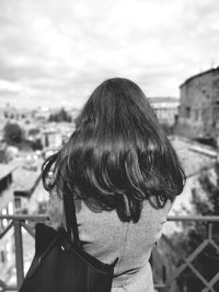 Rear view of woman standing against sky in city