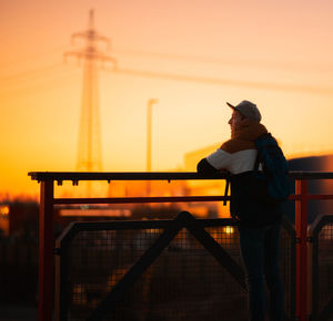 Man standing by railing against sky during sunset