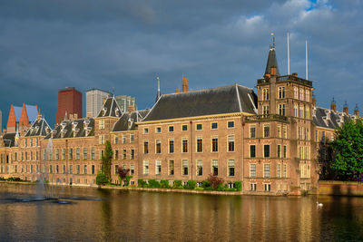 Buildings by river against cloudy sky