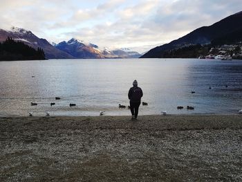 Rear view of person by lake against sky