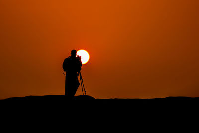 Silhouette man photographing against orange sky