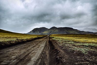 Dirt road leading towards mountains against sky