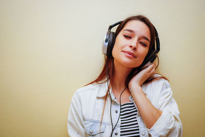 Young woman listening to music against wall