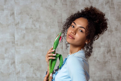 Portrait of smiling young woman holding tulip while standing against wall