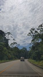 Cars on road by trees against sky in city