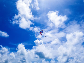 Low angle view of people paragliding against blue sky