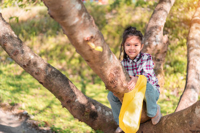 Portrait of smiling girl sitting on tree in forest