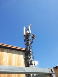 Low angle view of electrician repairing communications tower against blue sky