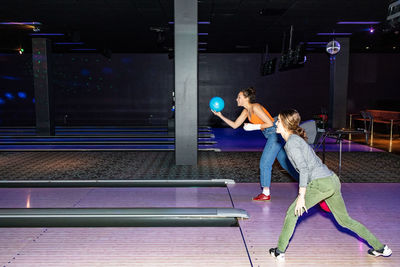 Full length of teenage girls throwing balls on parquet floor at bowling alley