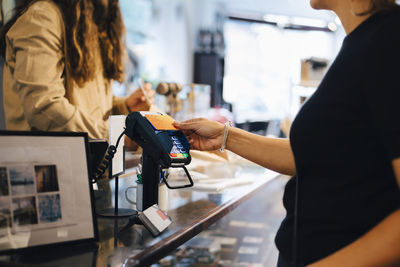 Cropped image of male customer paying through credit card to female owner at retail shop