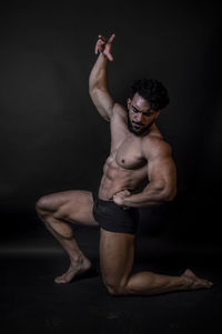 Shirtless man kneeling against black background