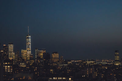 Illuminated buildings in city against clear sky at night