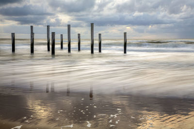 Wooden posts in sea against sky