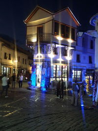 People on illuminated street against buildings at night