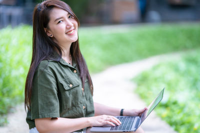 Young woman using laptop while sitting on field