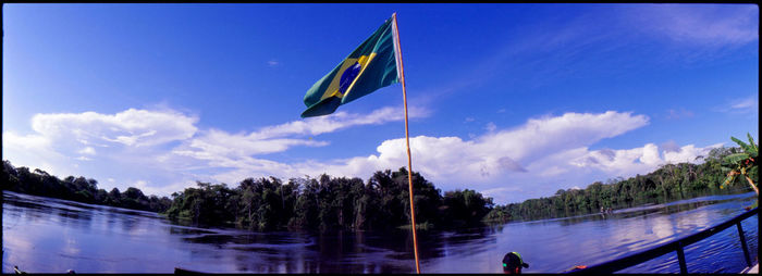 Panoramic view of flag by trees against blue sky