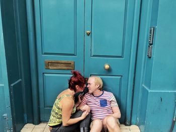 Full length of friends sitting on door