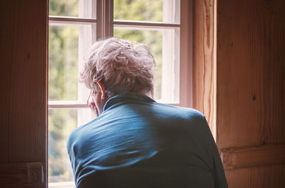 Rear view of man looking through window at home