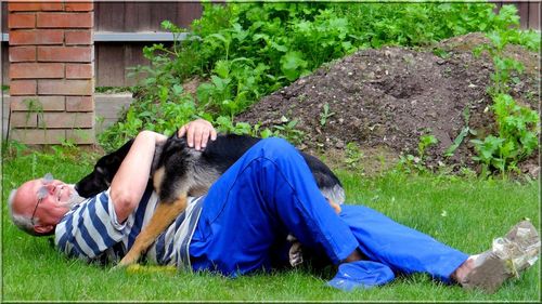 Full length of senior man playing with dog while lying on grassy field