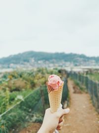 Hand holding ice cream cone against sky