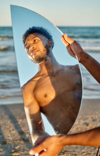 Crop african american male holding semicircular mirror while spending time on beach near sea