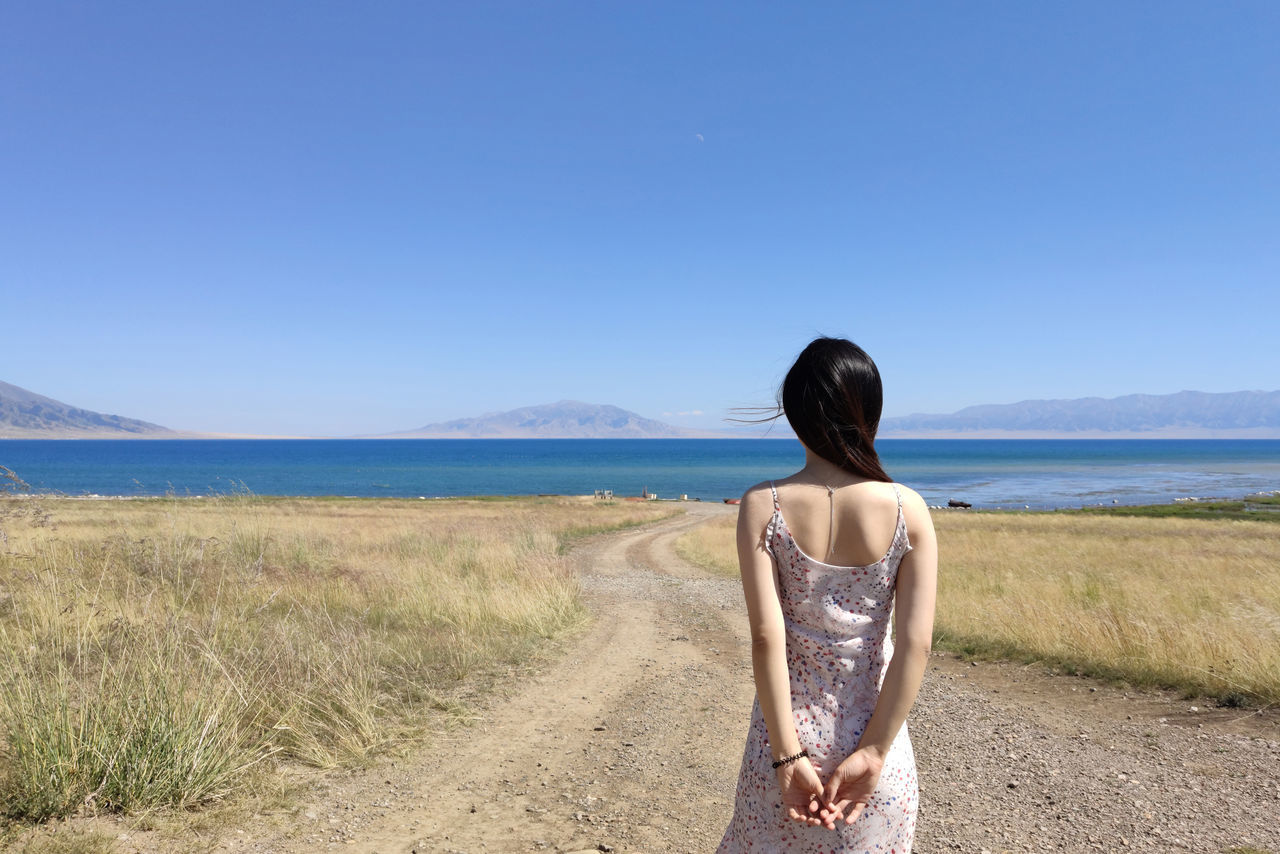 rear view, sky, one person, scenics - nature, land, nature, lifestyles, clear sky, beauty in nature, water, leisure activity, sea, hairstyle, day, women, copy space, casual clothing, blue, tranquility, standing, hair, outdoors