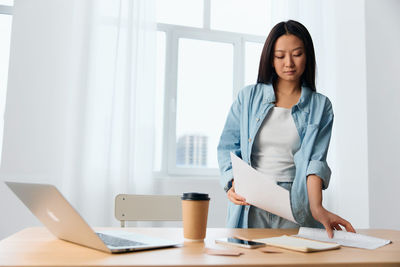 Young businesswoman holding documents by desk