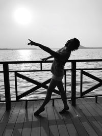 Full length of woman dancing by railing against sea