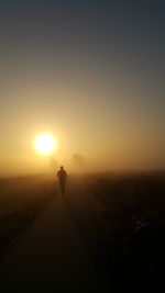 Silhouette man walking on landscape against sky during sunset